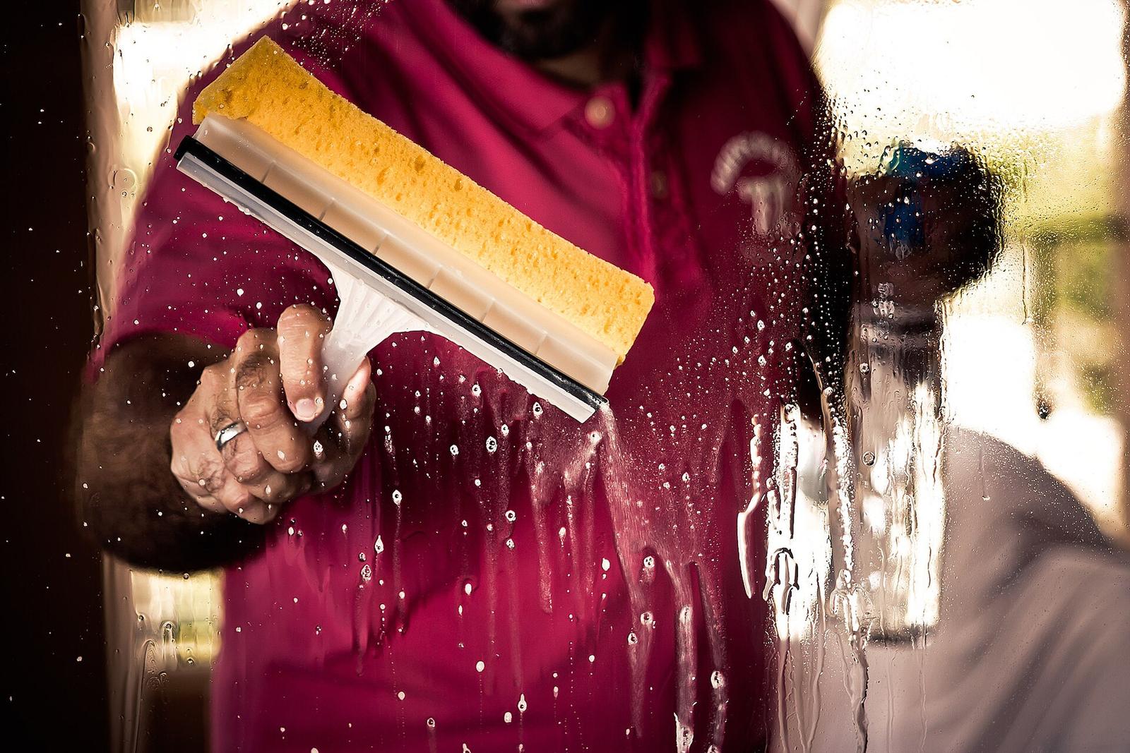 A window cleaner pulling a squeegee down a soapy pane of glass